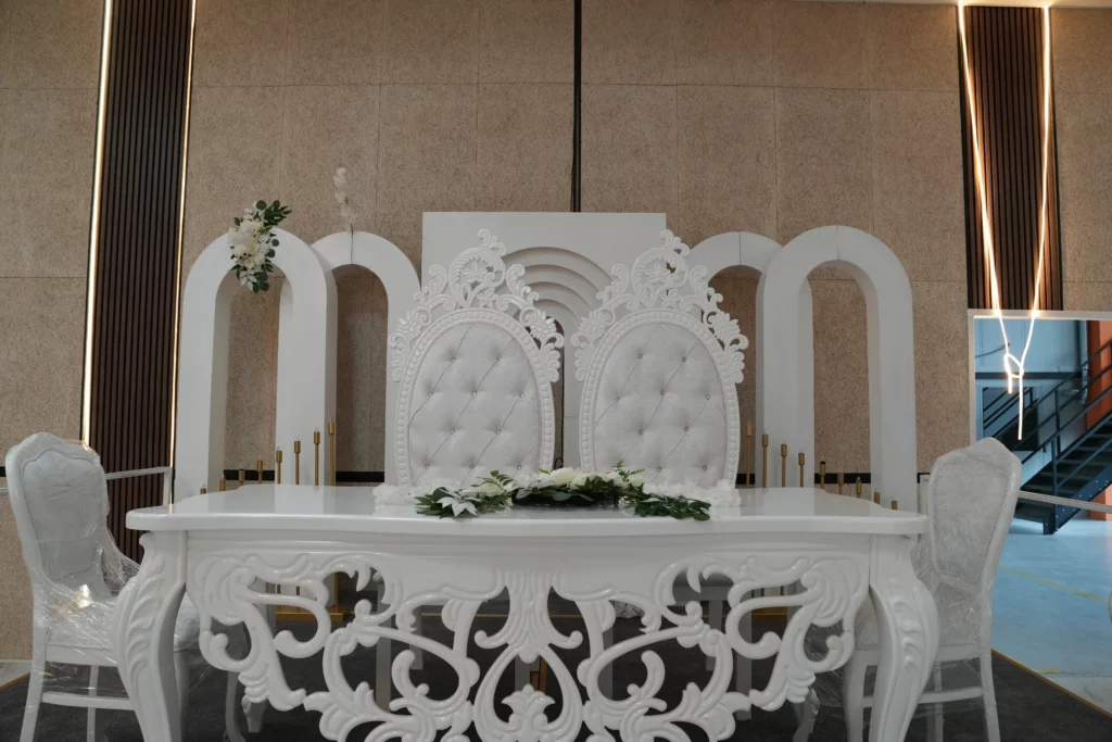 Bridal sweetheart table with ornate white throne chairs, floral garland and decorative arch backdrop at AWA Zug wedding venue