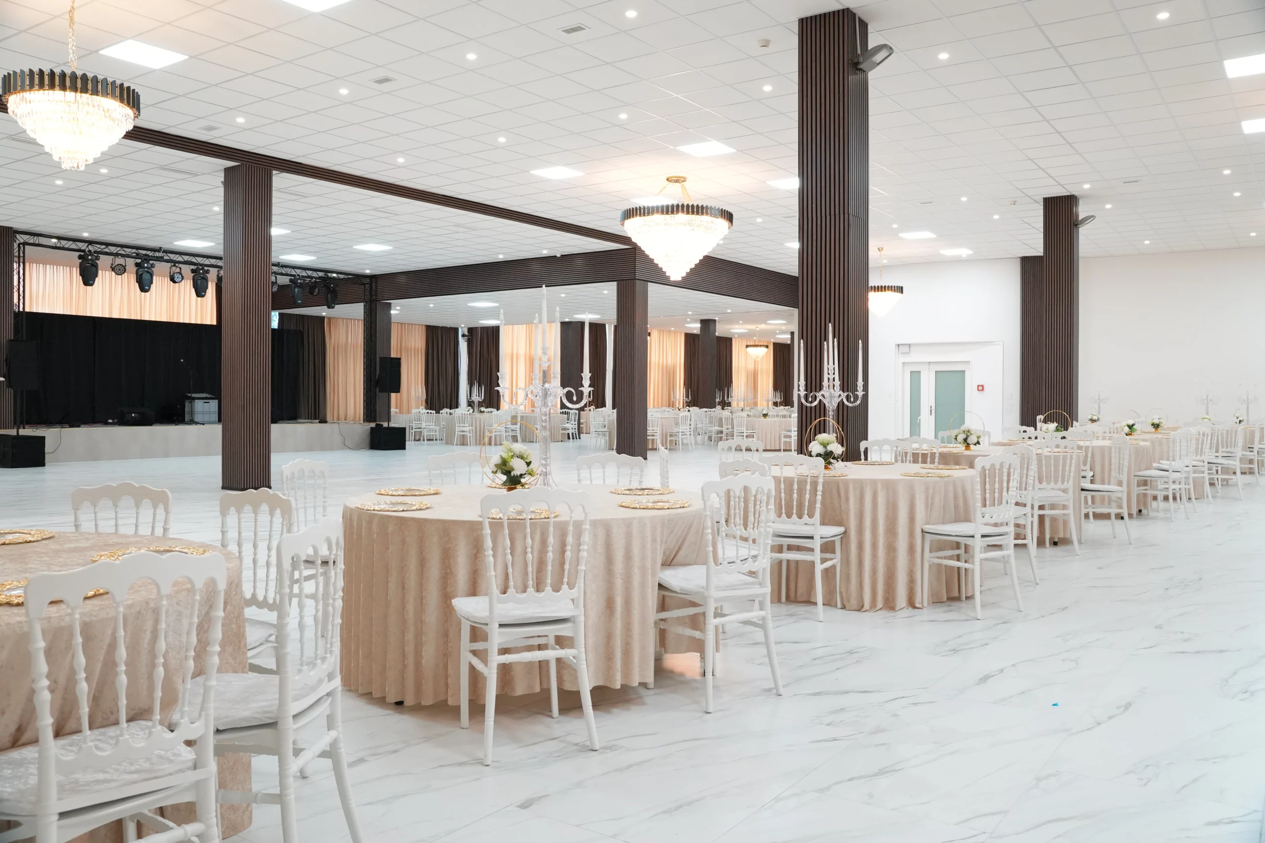 Grand ballroom with open dance floor, performance stage, crystal chandeliers and elegantly set tables at AWA Zug event venue