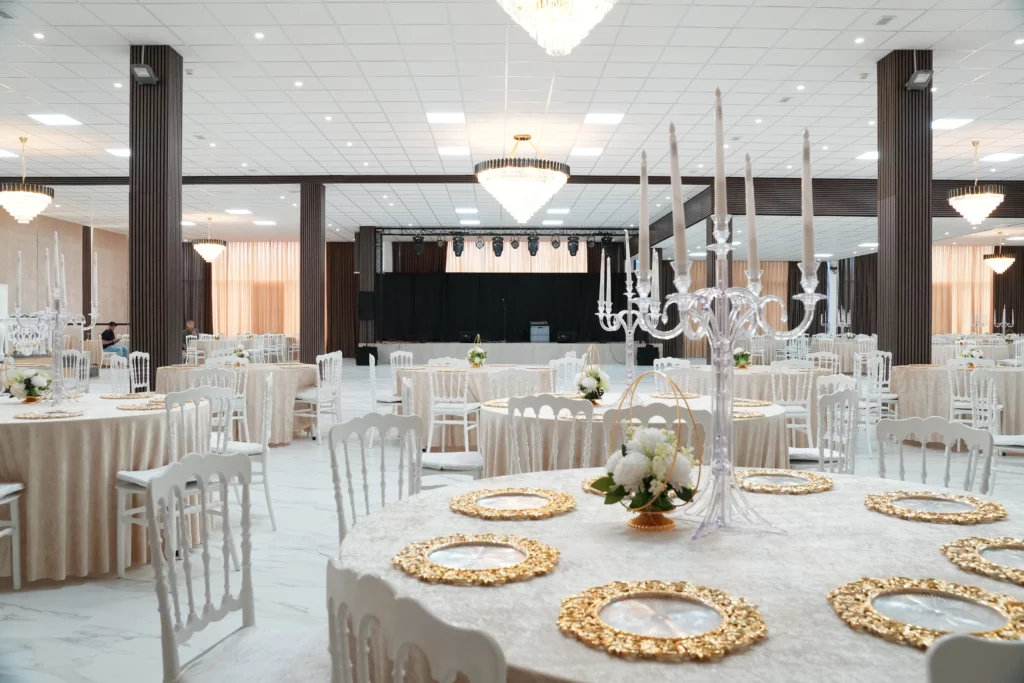 Large wedding venue hall with stage, round tables, ornate gold charger plates and crystal candelabras at AWA Zug event location