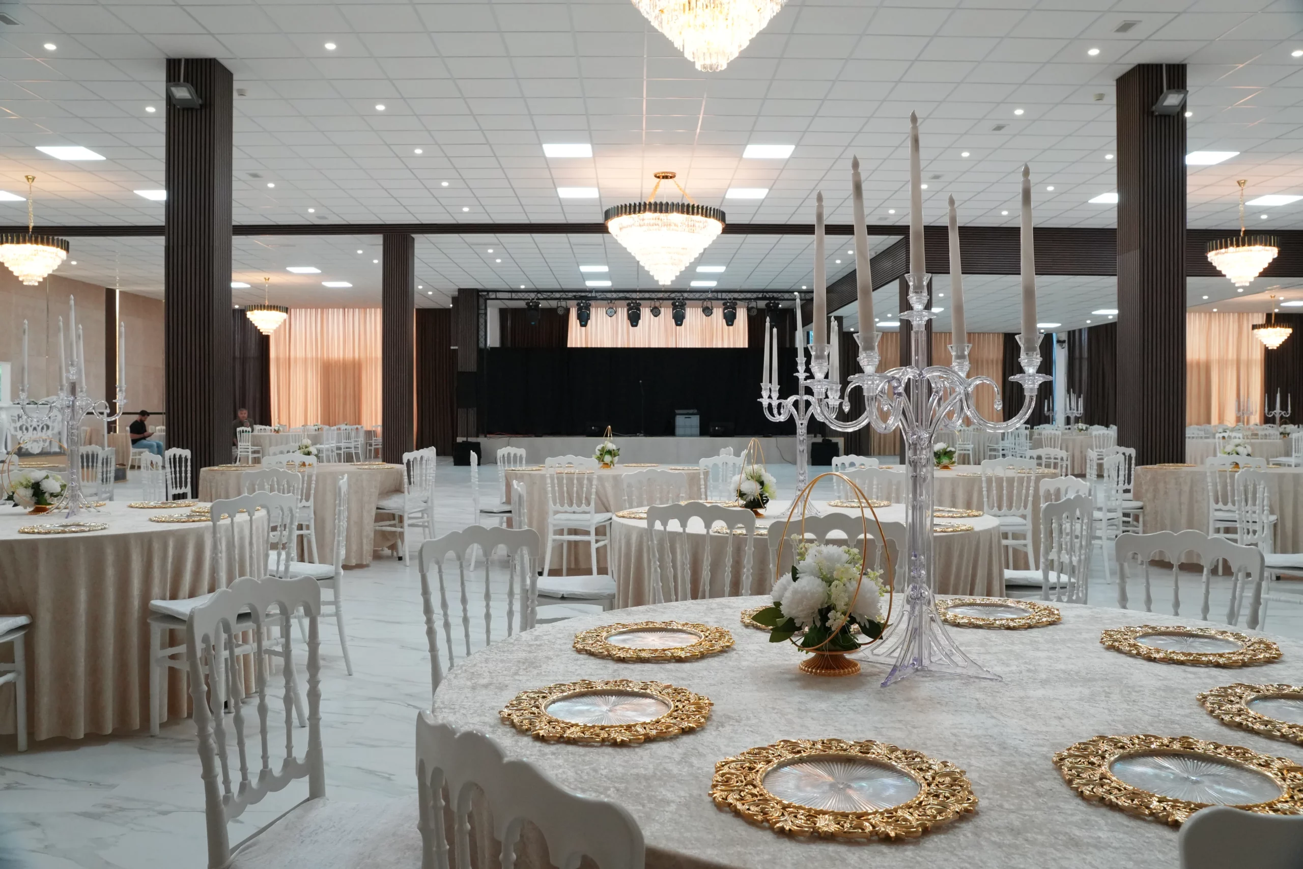 Large wedding venue hall with stage, round tables, ornate gold charger plates and crystal candelabras at AWA Zug event location