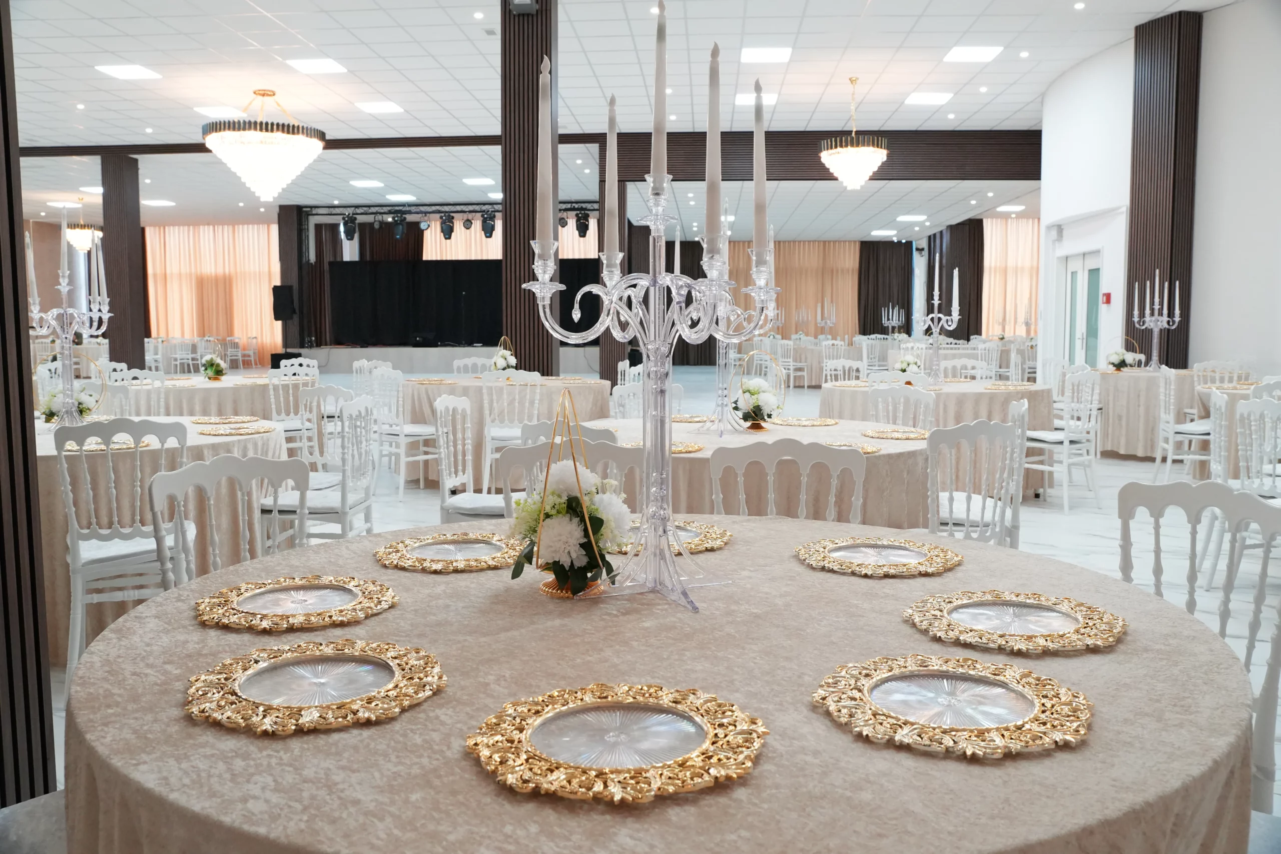 Large wedding venue hall with stage, round tables, ornate gold charger plates and crystal candelabras at AWA Zug event location