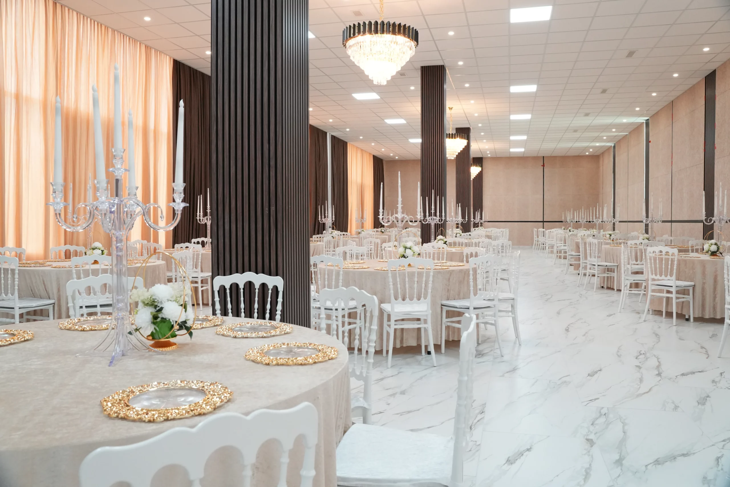 Elegant event hall with white Chiavari chairs, round tables, crystal chandeliers and marble floor at AWA Zug venue