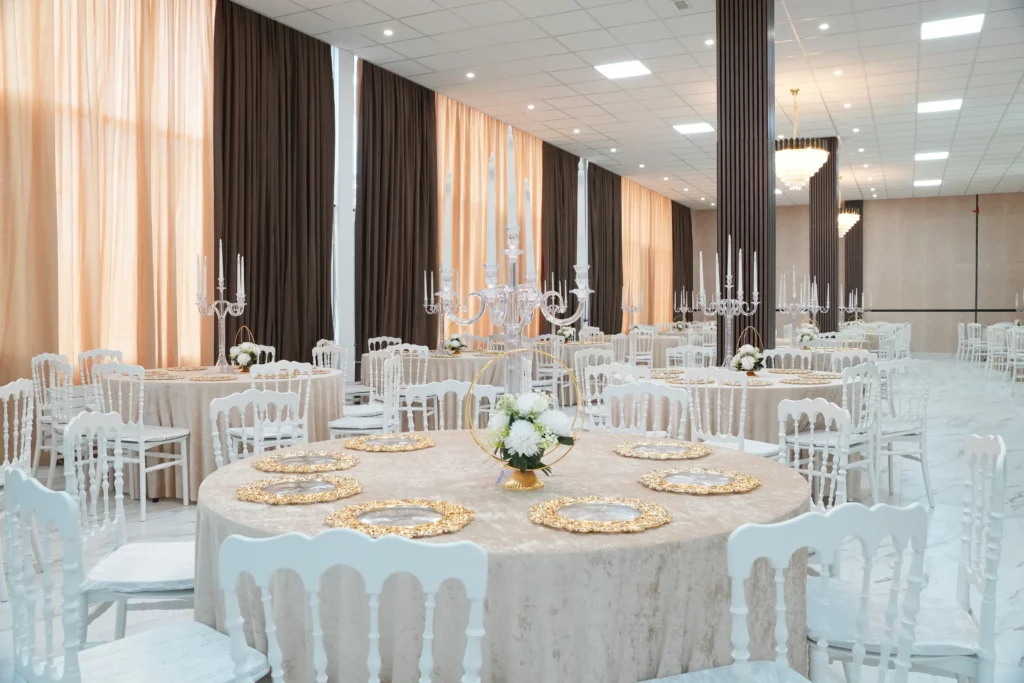 Wedding hall with mirrored walls, peach curtain backdrop, crystal chandelier and elegantly set round tables at AWA Zug Switzerland